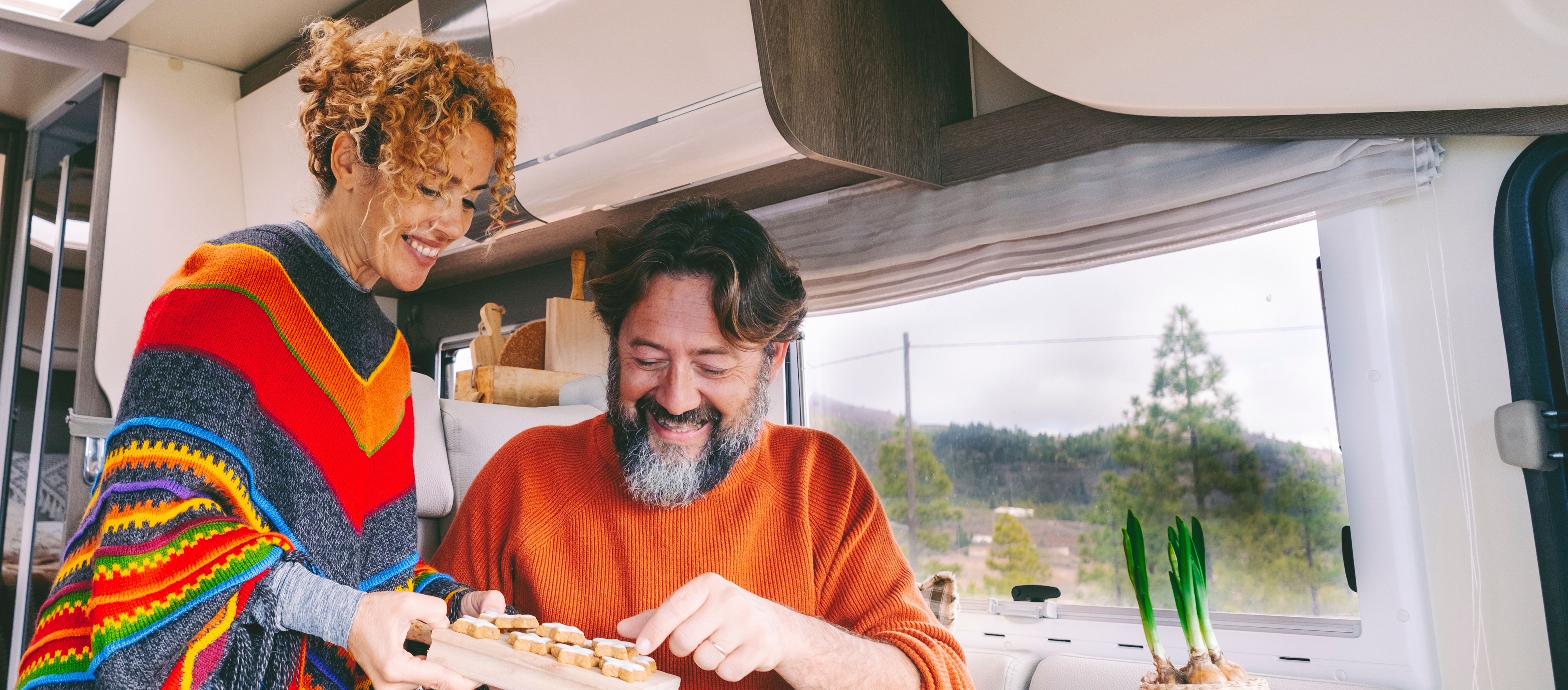 A happy middle-aged couple is eating cookies inside their RV bought with RV financing.